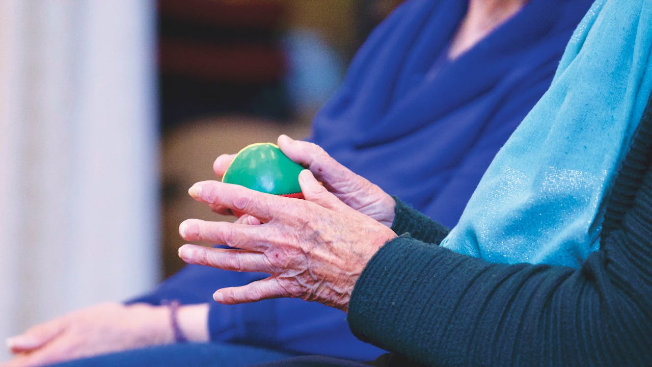 Close-up of senior person's hands holding a green therapy ball, showcasing wrinkles and care.